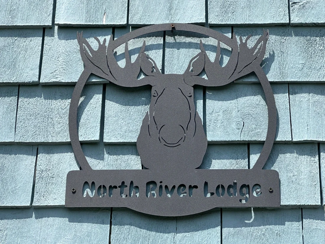 The hand-cut metal North River Lodge moose sign mounted on the home's blue cedar shingles