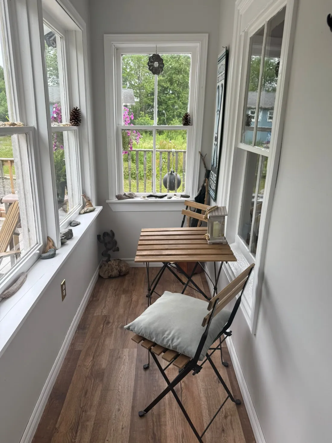 A bright enclosed sunroom with a wooden bistro table and windows overlooking the garden