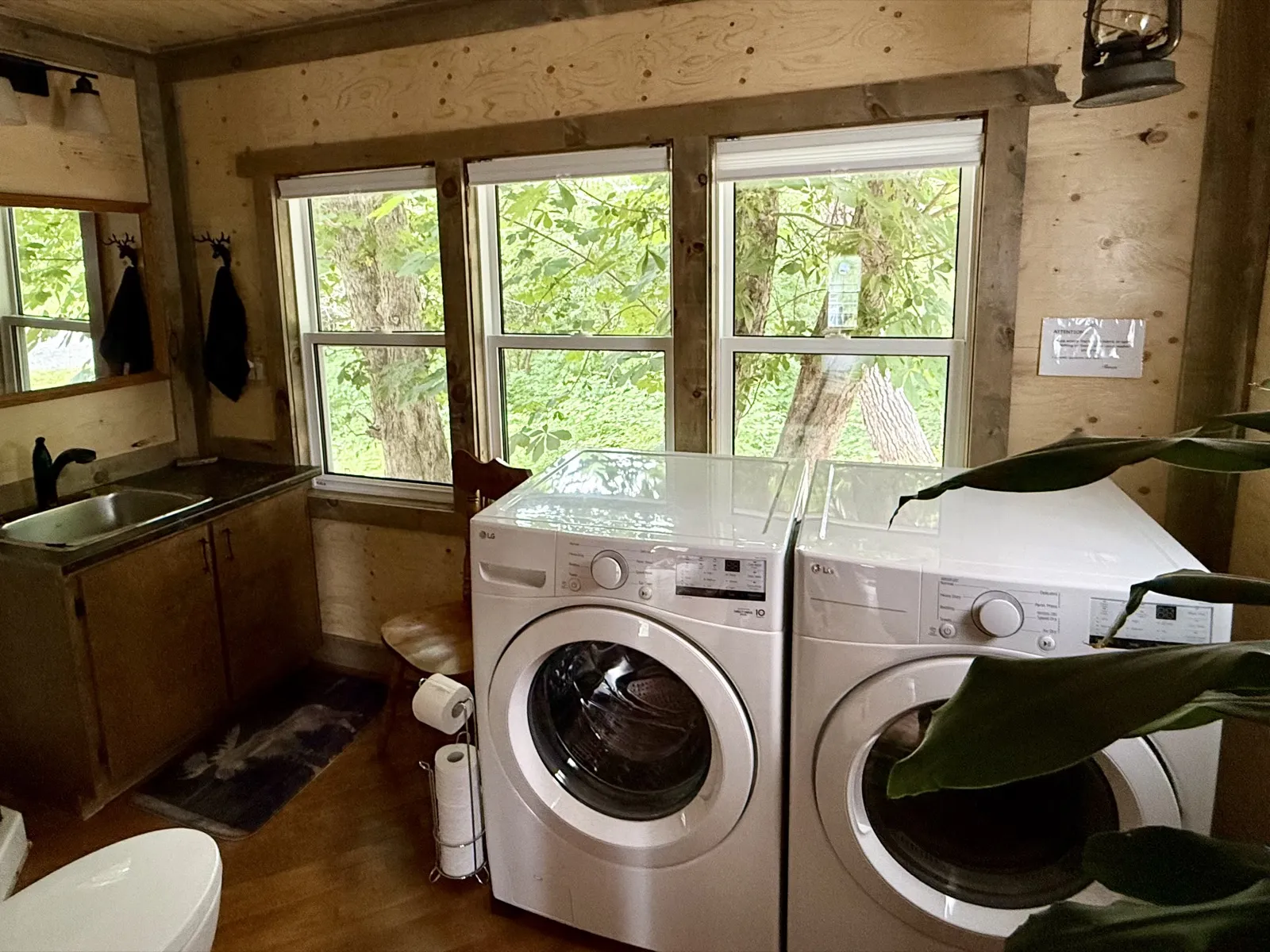 A modern front-load washer and dryer in a bright, wood-panelled room with windows to the trees