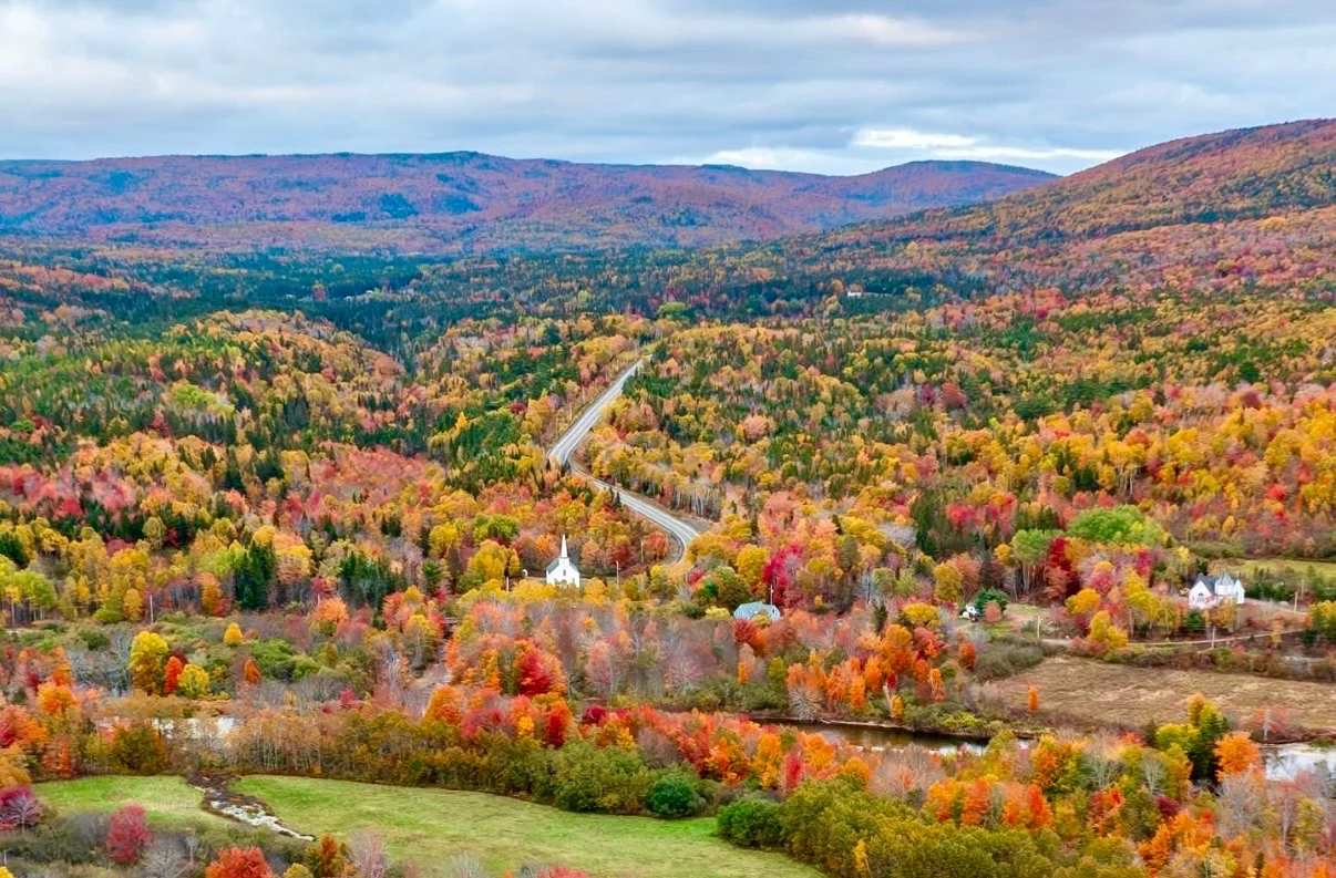 The Cabot Trail winding through fall-coloured highlands past a white church