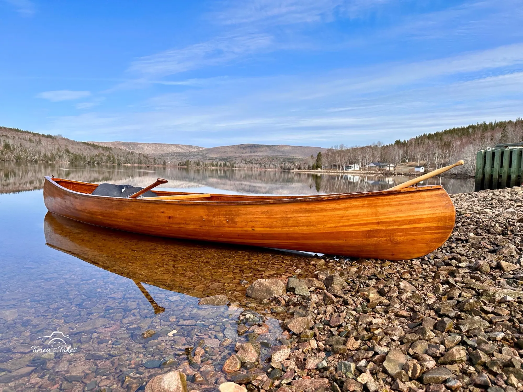 A handcrafted wooden canoe resting on the shore of a calm lake