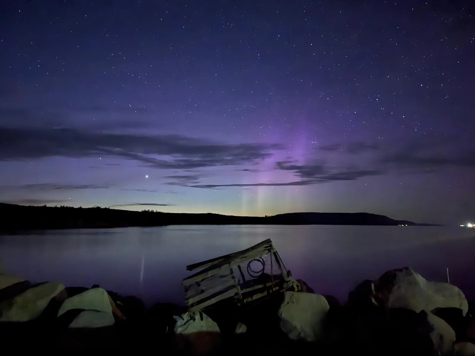 The northern lights glowing over a calm Cape Breton shoreline at night
