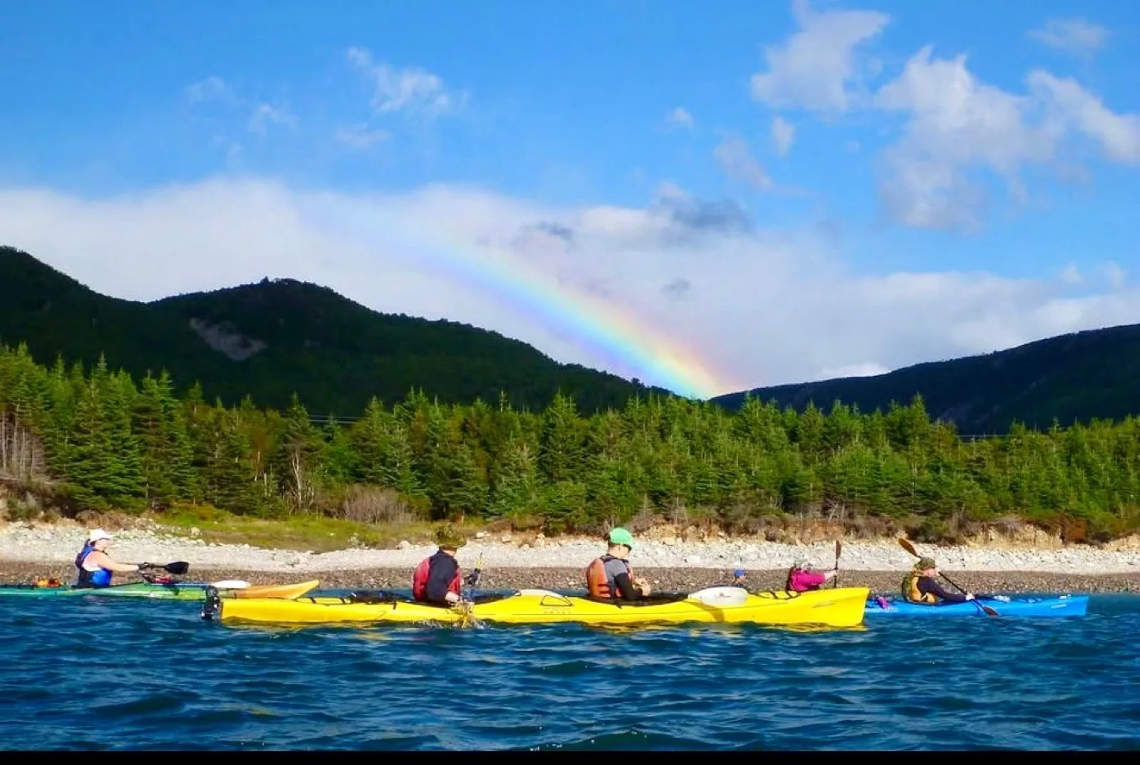 Sea kayakers paddling along the Cape Breton coast beneath a rainbow